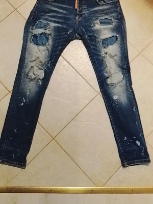 Dsquared2 jeans - Säljer ett par blå jeans från Dsquared2 med raka ben och slitna detaljer. Jeansen har klassisk femficksmodell, kontrastsömmar och en snygg tvättad look. Perfekta för dig som gillar streetwear och vill ha en cool vardagsstil.