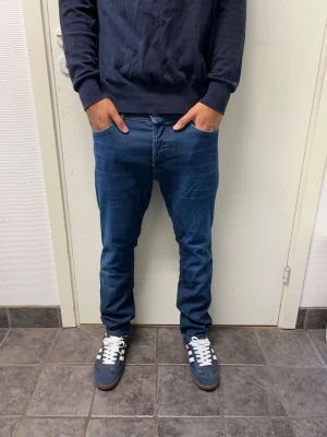 Jack & Jones jeans - Snygga mörkblå jeans från Jack & Jones. Mycket bra skick. Modell: Slim fit/Tim. A=40CM B=94CM C=17,5CM. Modellen är 173cm, 64kg. Pris kan diskuteras!!