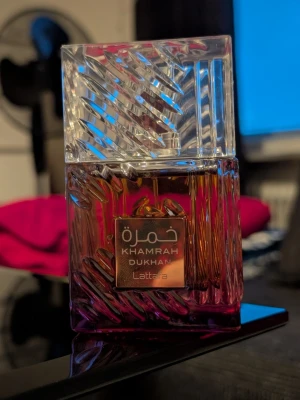 Lattafa Khamrah Dukhan Eau de Parfum 100ml - Säljer Lattafa Khamrah Dukhan (100 ml), den senaste och mörkaste flankern i serien. Flaskan är endast testsprayad. Detta är perfekta doften för dig som vill ha Khamrah-seriens lyxiga sötma, men med en mörkare twist av tobak, rökelse och kryddor. Flaskan har stått och mognat i en månad, vilket gjort doften mycket rundare och fylligare än en nyöppnad flaska.