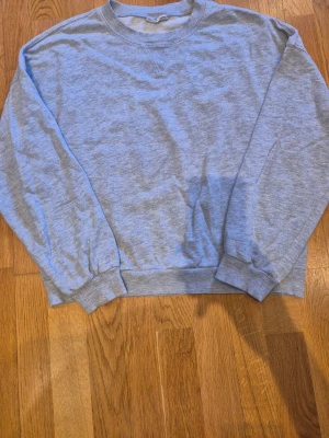 Grå sweatshirt från Gina Tricot - En klassisk ljusgrå sweatshirt från Gina Tricot, basically basics-kollektionen. Tröjan har rund hals, ribbade muddar vid ärmslut och nederkant samt en relaxed passform.