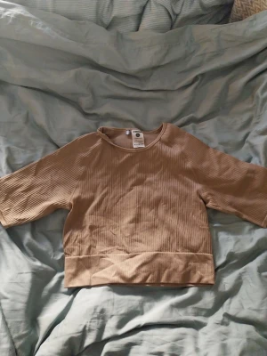 Beige ribbad topp från Stronger - Snygg beige ribbad topp från Stronger med bred mudd nertill och halvkort ärm. Tillverkad i mjukt material med 94% polyamid och 6% elastan för en skön och stretchig känsla. Perfekt för en avslappnad och trendig look. Eventuellt sportbh. Oanvänd. 