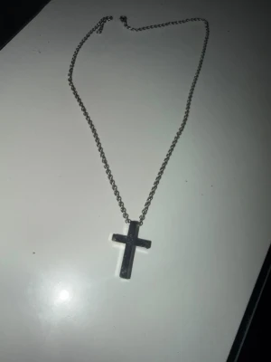 Silverfärgat halsband med kors - Snyggt halsband i silverfärg med ett klassiskt kors som hänge. Kedjan är tunn och enkel, vilket gör att korset står i fokus. Perfekt accessoar för dig som gillar stilrena smycken med en tidlös touch.
