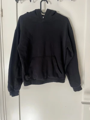 Svart basic hoodie med ficka - En svart hoodie i klassisk modell med huva och stor magficka framtill. Tröjan har ribbade muddar vid ärmslut och nederkant. 