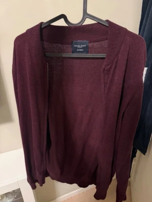 Vinröd kofta från Grand Frank - Stilren vinröd kofta från Grand Frank i tunt, mjukt material. Öppen framtill utan knappar eller dragkedja, perfekt att slänga på sig över en t-shirt eller skjorta. Långa ärmar och ribbade muddar ger en clean look.