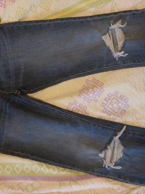 Mörkblå slitna jeans med hål - Snygga mörkblå jeans med slitningar och stora hål på båda knäna. Jeansen har en klassisk femficksmodell och är tillverkade i denim. Perfekta för en avslappnad och trendig look.