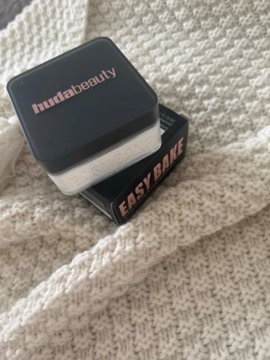 Huda Beauty Easy Bake Sugar Cookie - Huda Beauty Easy Bake i nyansen Sugar Cookie är ett löspuder i en fyrkantig plastburk med svart lock och rosa logga. Färgen är ljus och transparent, perfekt för att fixera basen och ge en matt finish.