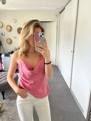 Rosa linnetopp med draperad urringning - Snygg rosa linnetopp med draperad v-ringad urringning och tunna axelband. Perfekt för varma dagar och enkel att styla med jeans eller kjol. Toppens material har en lätt glans och känns mjuk mot huden.