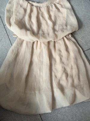 Beige offshoulder blus i chiffong - Luftig och söt beige offshoulder blus i tunn chiffong med lätt rynk vid halsringningen. Perfekt för en trendig och avslappnad look. Blusen har ett flowy fall och är lätt transparent.