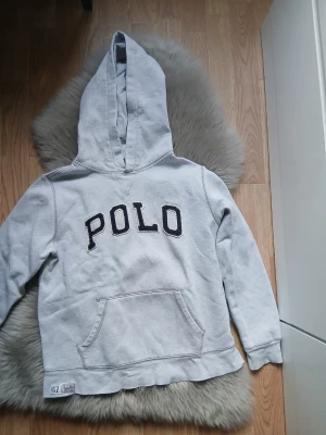 Grå hoodie från Polo Ralph Lauren - Snygg grå hoodie från Polo Ralph Lauren med stor huva och svart broderad POLO-text på bröstet. Perfekt för dig som vill ha en fräsch look och en avslappnad stil. Skick 7/10
