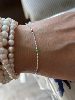 Tunt silverarmband med färgade pärlor - Ett stilrent och tunt armband i äkta silver (925) med små silverkulor och inslag av färgade pärlor i rött, grönt, blått och gult. Perfekt för dig som gillar minimalistiska smycken med en färgglad twist.liknar syster p armband Santa Monica 
