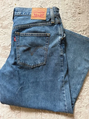Levi's raka blå jeans - Klassiska blå jeans från Levi's med rak passform och hög midja. Jeansen har fem fickor, synliga sömmar och ikonisk läderpatch bak i midjan. Tillverkade i slitstark denim med vintagekänsla.
