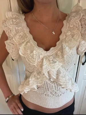Vit spetsblus med volanger - Supersöt vit blus med v-ringning och stora volanger i spets. Toppen har korta ärmar och är stickad med fina spetsdetaljer som ger en romantisk vibe. Perfekt att styla med jeans eller kjol för en trendig look.