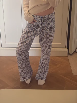 Mönstrade loungewear-byxor blå/vit - Säljer ett par mjuka loungewear-byxor med blått och vitt grafiskt mönster. Byxorna har rak passform, resår och dragsko i midjan för extra komfort. Perfekta för chill dagar hemma.