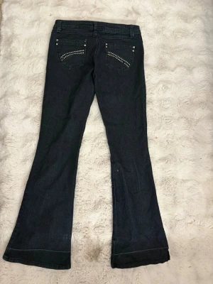 Bootcut jeans med nitar - Mörkblå bootcut jeans med coola nitar på fickorna. Klassisk femficksmodell och snyggt utsvängda ben. Perfekt för dig som gillar en lite retro stil och vill ha något som sticker ut. Materialet är denim och jeansen har en låg till normal midja.