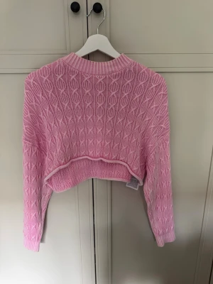 Rosa cropped stickad tröja XS - Säljer en rosa cropped stickad tröja från FB Sister i storlek XS. Tröjan har ett kabelstickat mönster, ribbad halsringning och muddar. Helt ny