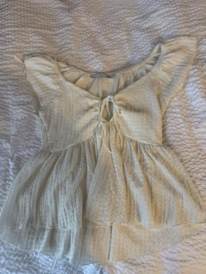 Ljus blus med knyt - Söt ljus blus med korta ärmar och knyt framtill. Blusen har en lätt volang nedtill och är tillverkad i ett tunt, luftigt tyg som ger en romantisk känsla. Perfekt för varma dagar och enkel att styla till olika looks. Är storlek S men passar en M