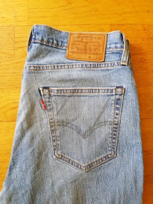 Levi's 511 ljusblåa raka jeans  - Säljer ett par klassiska ljusblå jeans från Levi's med raka ben och ikonisk läderpatch bak i midjan. Jeansen har en bakficka med den röda Levi's-taggen och är tillverkade i slitstark denim. Perfekta för en avslappnad och tidlös stil.