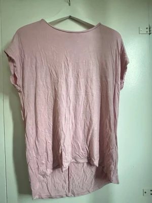 Ljusrosa loose topp i bomull - Enkel och snygg ljusrosa topp med loose passform och rund halsringning. Toppen är ärmlös och har längre bakstycke för en avslappnad look. Perfekt att styla med jeans eller kjol. Är en stor xs.