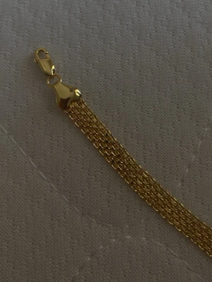 Guld färgat  kedjearmband i flera rader - Snyggt armband i guldfärgad metall med flera tunna kedjor som ger en elegant och modern look. Armbandet har ett smidigt klolås och passar perfekt för dig som gillar stilrena accessoarer. Perfekt att bära ensam eller att matcha med andra smycken.