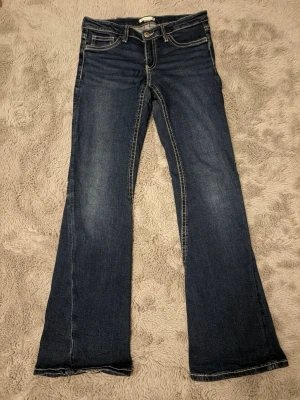 Bootcut jeans från Gina Tricot Young - Snygga mörkblå bootcut jeans från Gina Tricot Young med kontrastsömmar och klassisk femficksdesign. Jeansen har en lätt utsvängd passform och är tillverkade i denim med en cool tvätt. Perfekta för en trendig och avslappnad look. I storlek 164 barn