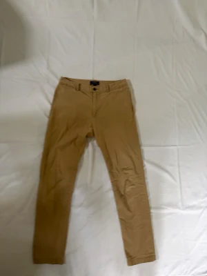 Beiga chinos från Polo Ralph Lauren - Säljer ett par klassiska chinos från Polo Ralph Lauren i beige/khaki färg. Stilren och tidlös modell som passar perfekt till både vardag och mer uppklädda outfits. Diskreta detaljer med broderad Polo-logga baktill och knäppbara bakfickor. Märke: Polo Ralph Lauren Färg: Beige / Khaki Modell: Chinos Passform: Slim/rak passform Skick: Bra använt skick Detaljer: Zip-gylf, knappstängning, klassisk preppy stil