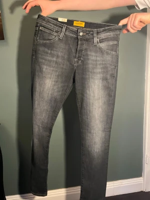 Grå slim fit jeans från Jack and Jones  - Slim fit jeans i grå tvätt från Hollister med klassisk femficksdesign och diskreta slitningar. Jeansen har normal midja, smal passform och är tillverkade i stretchigt denim för extra komfort. Perfekta för en avslappnad och trendig look. Nypris ca 1000 kr