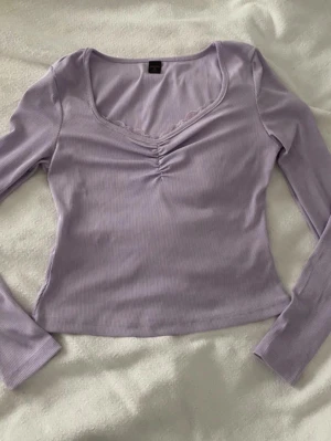 Ljuslila ribbad topp från Romwe - Supersöt ljuslila långärmad topp från Romwe med ribbad struktur och v-ringning. Toppen har spets detaljer vid bysten och en feminin passform. Perfekt att styla med jeans eller kjol för en trendig look.