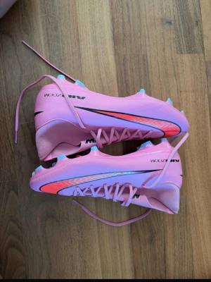 Nike Air Zoom rosa fotbollsskor - Säljer ett par Nike Air Zoom fotbollsskor i en snygg rosa färg med svarta och röda detaljer..Perfekta för dig som vill sticka ut på planen och ha grymt grepp. Helt nya aldrig använda 