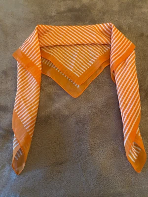 Orangevit randig sjal vintage - Snygg sjal i tunn, lätt kvalitet med orange och vita ränder. Sjalen är fyrkantig och har en bred orange kant runt om. Perfekt att knyta runt halsen eller i håret för en fräsch look.