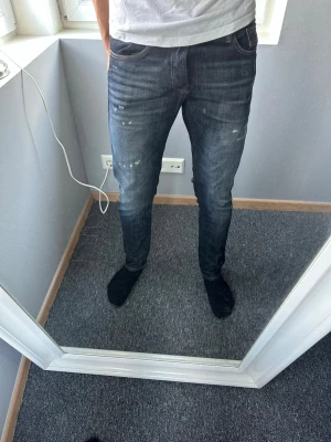Mörkblå slim fit jeans med slitningar - Säljer ett par mörkblå slim fit jeans med lätt slitna detaljer och diskreta färgstänk. Jeansen har klassisk femficksdesign och smal passform som sitter snyggt längs benen. Perfekta för en trendig och avslappnad look.