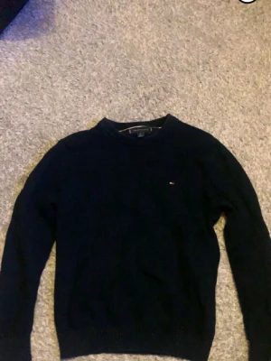 Tommy Hilfiger tröja - mörkblå stickad tröja från Tommy Hilfiger med rund halsringning och  logga på bröstet. Tröjan är i bra skick och har inga defekter. Hör av dig vid frågor och funderingar