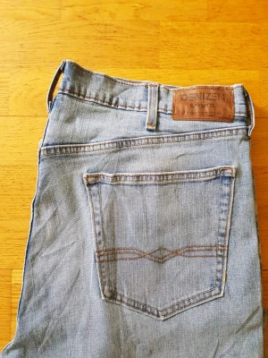 Levi's Denizen ljusblåa jeans  - Snygga ljusblå jeans från Denizen by Levi's med klassisk femficksdesign och bruna sömmar. Jeansen har en rak passform och är tillverkade i slitstarkt denim. Perfekta för en avslappnad och trendig look.