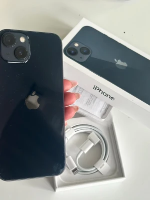iPhone 13 Midnight 128GB med box - Säljer en svart iPhone 13 med 128GB lagring. Telefonen har en stilren design i glas och aluminium, dubbla kameror på baksidan och levereras med originalkartong och USB-C till Lightning-kabel. Perfekt för dig som vill ha en snabb och snygg mobil från Apple.