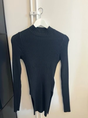 Svart ribbad stickad polotröja NA-KD - Säljer en svart, figurnära stickad tröja med ribbad struktur och hög hals. Tröjan har långa ärmar och är tillverkad i ett stretchigt material som sitter snyggt på kroppen. Använd endast 2 ggr och har inga defekter. Pris går att diskutera vid snabb affär😊