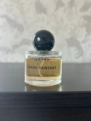 NAIYA Dark Fantasy parfym - NAIYA Dark Fantasy är en elegant parfym i en rund, genomskinlig glasflaska med svart klotformad kork. Doften har en lyxig känsla och flaskan har en stilren design med svart text. Perfekt för dig som gillar snygga och moderna parfymer. Doften är inspirerad an Born in Roma. Säljer då jag har för många parfymer.