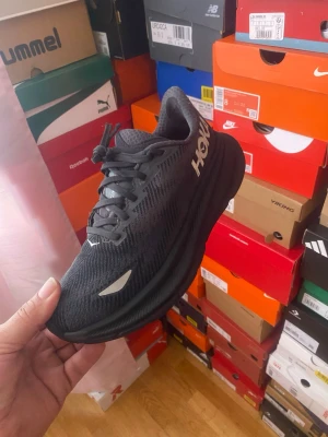 Svarta Hoka sneakers med Gore-Tex - Snygga svarta sneakers från Hoka med Gore-Tex-material som gör dem vattentäta. Skorna har en sportig design med mesh-överdel, tjock sula och Hoka-logga på sidan. Perfekta för dig som vill ha stilrena och funktionella sneakers.