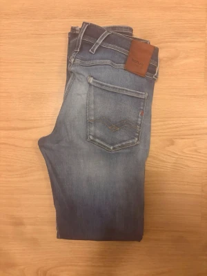 Replay jeans - Snygga blå jeans från Replay med klassisk femficksdesign och slim passform. Jeansen har ljusa slitningar och en läderpatch med Replay-logga bak i midjan. Perfekta för dig som gillar en avslappnad men trendig stil.