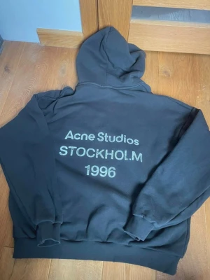 Svart hoodie Acne Studios Stockholm - Svart hoodie från Acne Studios med tryck på ryggen. Klassisk modell med luva och ribbade muddar.