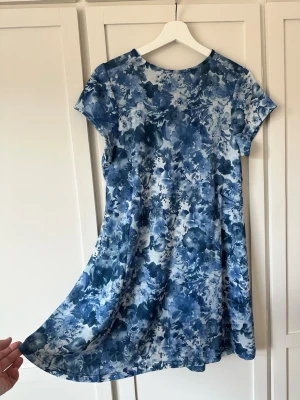 Blå blommig sommarklänning - Supersöt klänning med blått blommönster och rund hals. Klänningen har korta ärmar och ett lätt utställt fall. Köpt i Spanien i butik liknande Bershka/Stradivarius. Märkeslapp saknas, men uppskattas passa S / M.                                       Mått: • Längd ca 84–85 cm • Axel Axel till axel ca 35–36 cm Ärmarna är avkortade för en nättare look, se närbild på sömmen.  Endast använd 1–2 gånger — jättefint skick.   