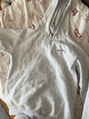 Grå hoodie med tryck Ma chérie - Snygg ljusgrå hoodie med huva och trycket 'Ma chérie' på bröstet och ett större hjärttryck med pil på ryggen. Mjuk bomullsmix och ribbade muddar. Perfekt för en chill och trendig look.
