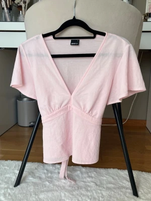 Ljusrosa topp - Supersöt ljusrosa topp från Gina Tricot med djup v-ringning och knyt i midjan. Den har korta och vida ärmar. Endast använd ett fåtal gånger💗