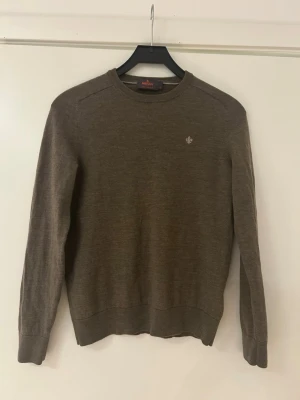 Brun merinoullströja från Morris - Snygg brun tröja från Morris i mjuk merinoull. Klassisk rund halsringning och diskret Morris-logga broderad på bröstet. Långärmad modell med ribbade muddar vid ärmslut och nederkant. Perfekt för lager på lager och stilren look. Passformen är lite liten så passar mer S