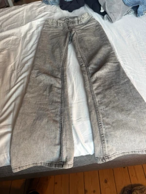 Gråa utsvängda jeans - Säljer ett par gråa jeans med utsvängda ben och klassisk femficksmodell. Jeansen har en snygg tvättad look och är tillverkade i denim med skön stretch. Perfekta för dig som gillar retrostil och vill ha ett par statement-jeans i garderoben.