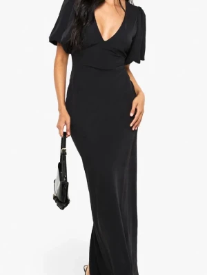 Svart långklänning med v-ringning - Elegant svart långklänning med djup v-ringning och korta, lösa ärmar. Klänningen har en smickrande passform och är tillverkad i ett mjukt, följsamt material som ger ett stilrent intryck. Perfekt för dig som vill ha en klassisk och tidlös look.