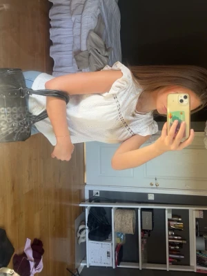 Vit ärmlös blus med broderade detaljer - Säljer en söt vit blus med broderade hål och volang vid axlarna. Blusen är ärmlös och har en avslappnad passform som ger en luftig känsla. Perfekt till jeans eller kjol för en fräsch look.