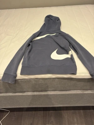 Mörkblå Nike hoodie med dragkedja - Snygg mörkblå hoodie från Nike med vit dragkedja och stora vita swoosh-loggor på både fram- och baksidan. Tröjan har huva och två fickor framtill. Tillverkad i mjukt bomullsmaterial för extra komfort.