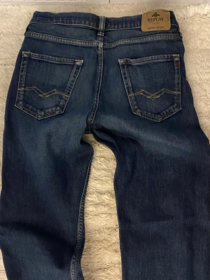 Mörkblå Thad jeans från Replay - Snygga mörkblå jeans från Replay med klassisk femficksmodell och kontrastsömmar på bakfickorna. Jeansen har en rak passform och är tillverkade i slitstarkt denimtyg. Perfekta för en avslappnad och trendig look.