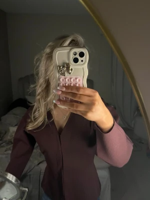 Vinröd blus med v-ringning - Snygg vinröd blus med v-ringning och ballongärmar. Blusen har en figurnära passform och är tillverkad i ett glansigt material som ger en lyxig känsla. Perfekt att styla med jeans eller kjol för en trendig look.