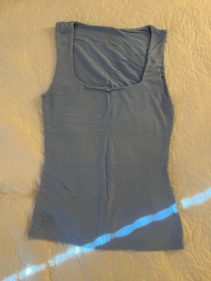 Ljusblå ribbad tanktop - Säljer en ljusblå ribbad tanktop från H&M med breda axelband och djup rundad halsringning. Materialet är mjukt och stretchigt, perfekt för att matcha med jeans eller shorts. Enkel och stilren design som passar till många olika outfits.