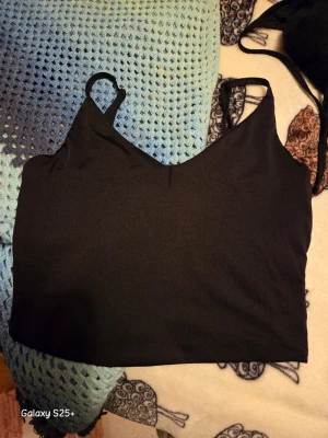 Svart croppad linnetopp - Snygg svart croppad linnetopp med smala axelband och v-ringad hals. Perfekt att styla med höga jeans eller kjol för en trendig look. Enkel och stilren design som passar till många outfits.